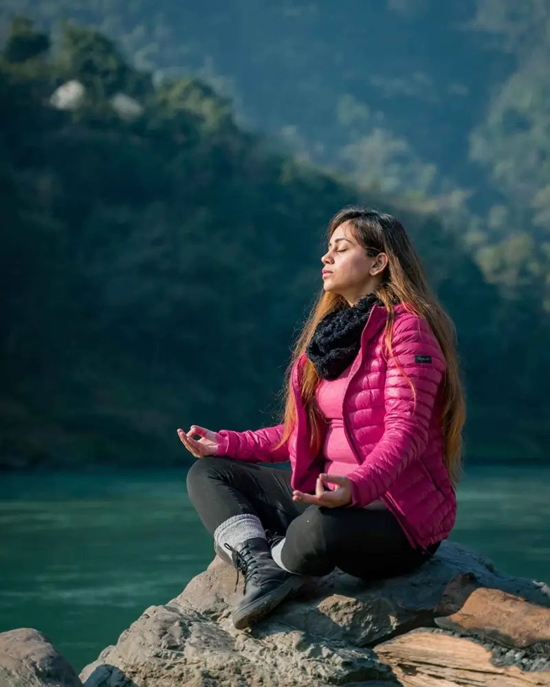 Student performing pranayama meditation by a riverside in nature