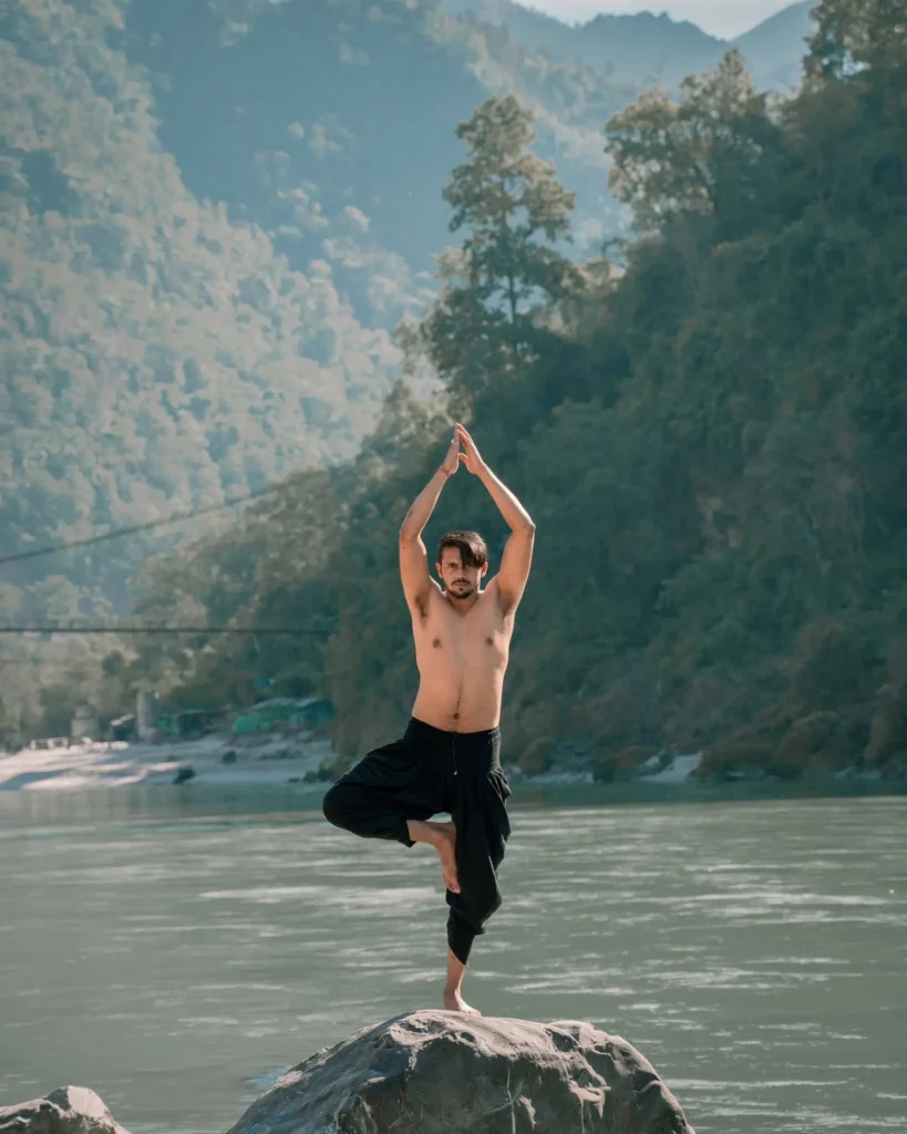 Vrikshasana tree pose yoga by the Ganges river in Rishikesh, India